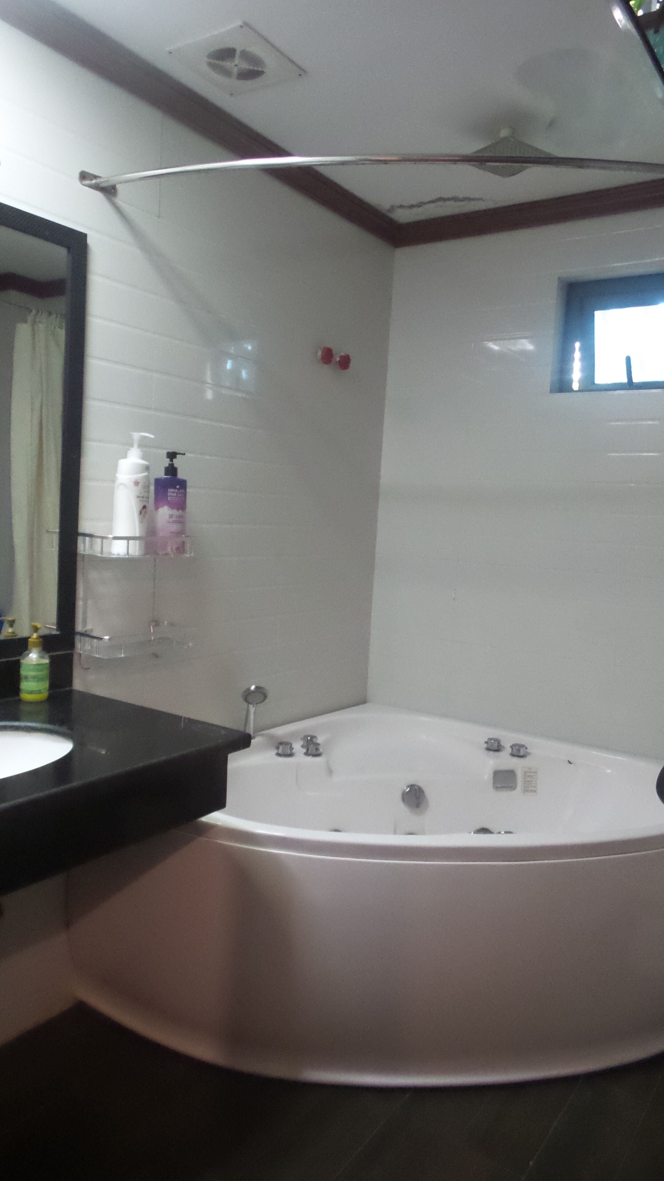 A bathroom with a white bathtub, a black countertop, a mirror, and a window.