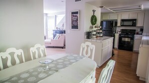 Ein Essbereich mit Tisch und Stühlen, eine Küche mit Geräte und ein Wohnzimmer im Hintergrund.