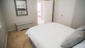 Ein Schlafzimmer mit Bett, Kommode, Spiegel und einer Tür zu einem anderen Raum.