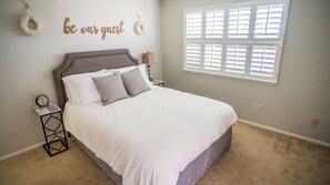 A bedroom with a bed, a nightstand, a wall clock, and a window with blinds. - Vintage Paso by Avantstay Firepit + Garden + BBQ Walk to Downtown Paso (Paso Robles)