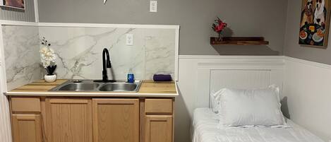 Una habitación compacta con kitchenette, cama y un adorno floral en la pared.