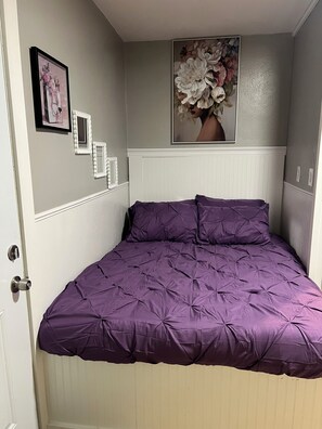 Ein Schlafzimmer mit einem Bett, einer Tür, einer Wand mit gerahmten Bildern und einem floralen Gemälde.
