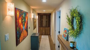 A hallway with a wooden door, a wall-mounted wreath, and a painting. - Hilltop West by Avantstay Deck Grill + Game Lounge Paso Robles Wine Country (Paso Robles)