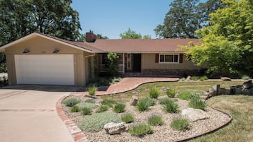 A single-story house with a garage, a covered porch, and a landscaped front yard with rocks and plants.