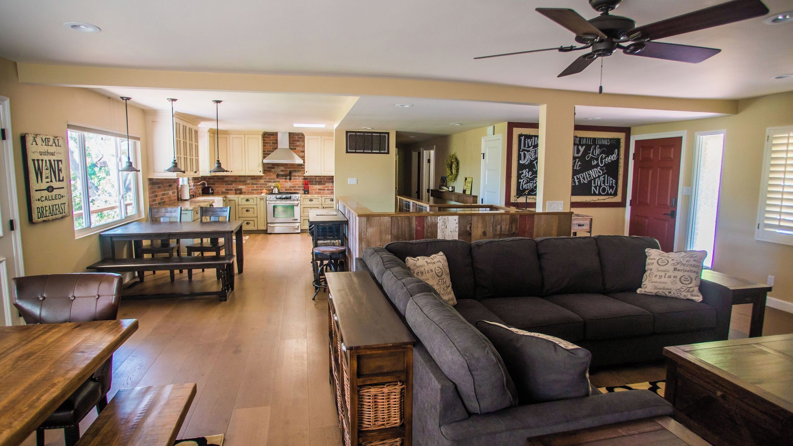 A spacious living area with a dark grey sofa, wooden dining table, and a kitchen in the background.