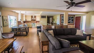 A spacious living area with a dark grey sofa, wooden dining table, and a kitchen in the background.
