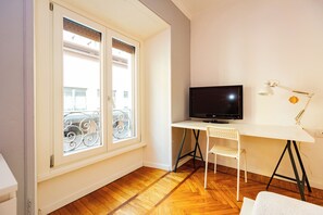 A room with a TV on a desk, a chair, a window with a view of buildings, and a white wall. - Buenosaires5 Elegance in Porta Venezia by Hospity (Milan)