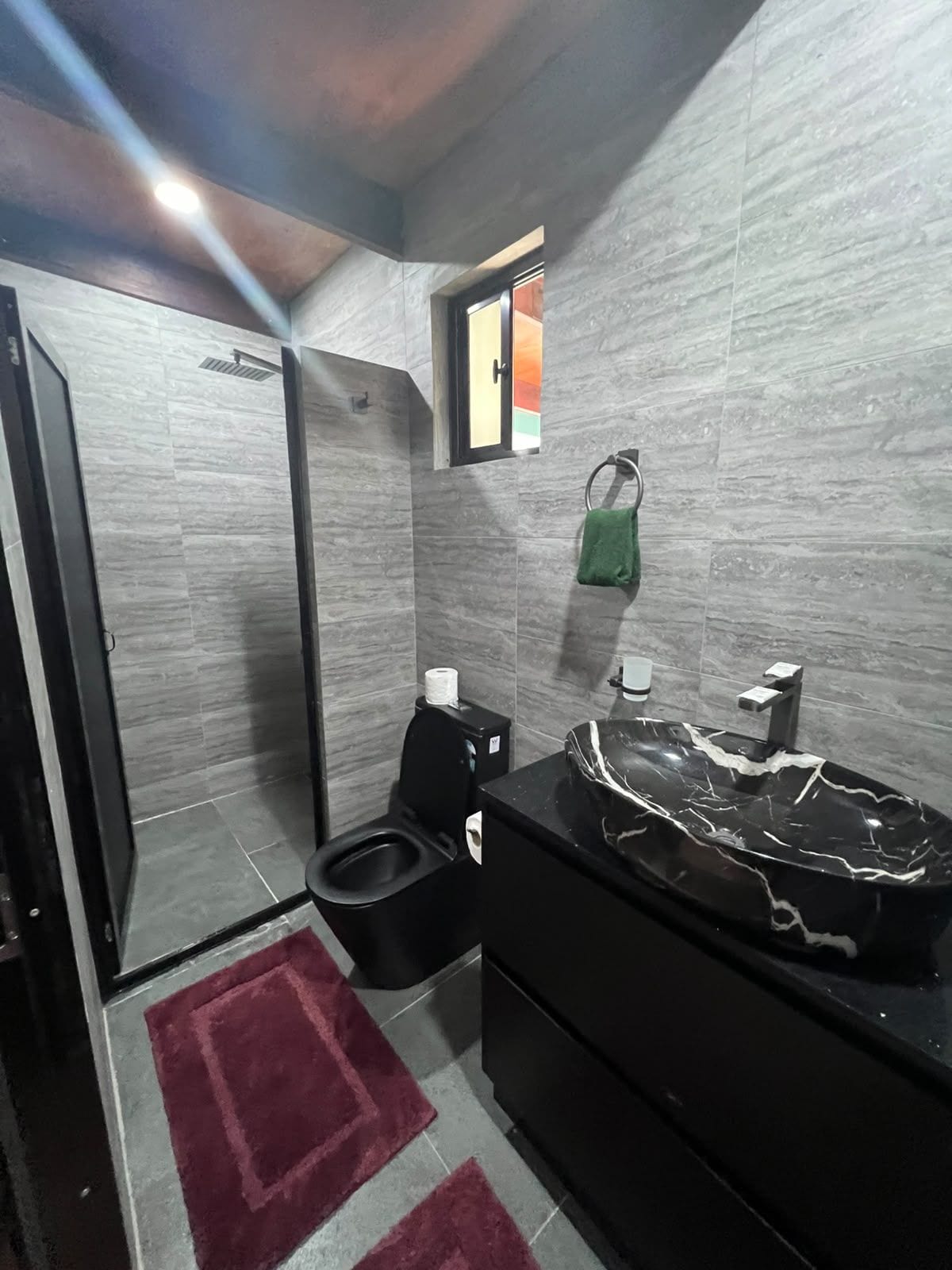Een badkamer met een zwart toilet, een marmeren wastafel en een rode vloerkleed.