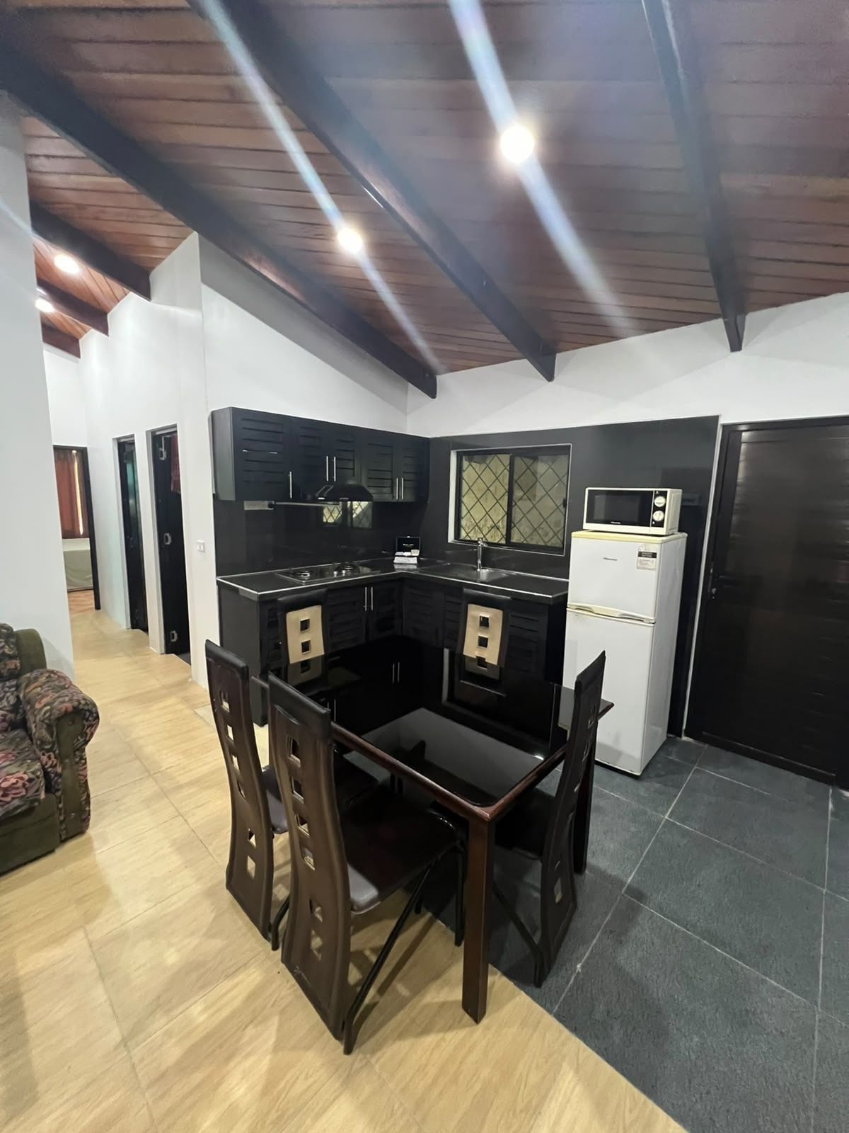 Una cocina moderna con muebles oscuros, una mesa de comedor con sillas y un refrigerador.