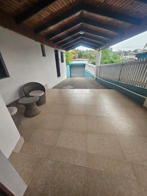 A covered outdoor area with tiled flooring, a seating arrangement, and a view of a building in the background. - Holiday Hire Fiji (Lautoka)