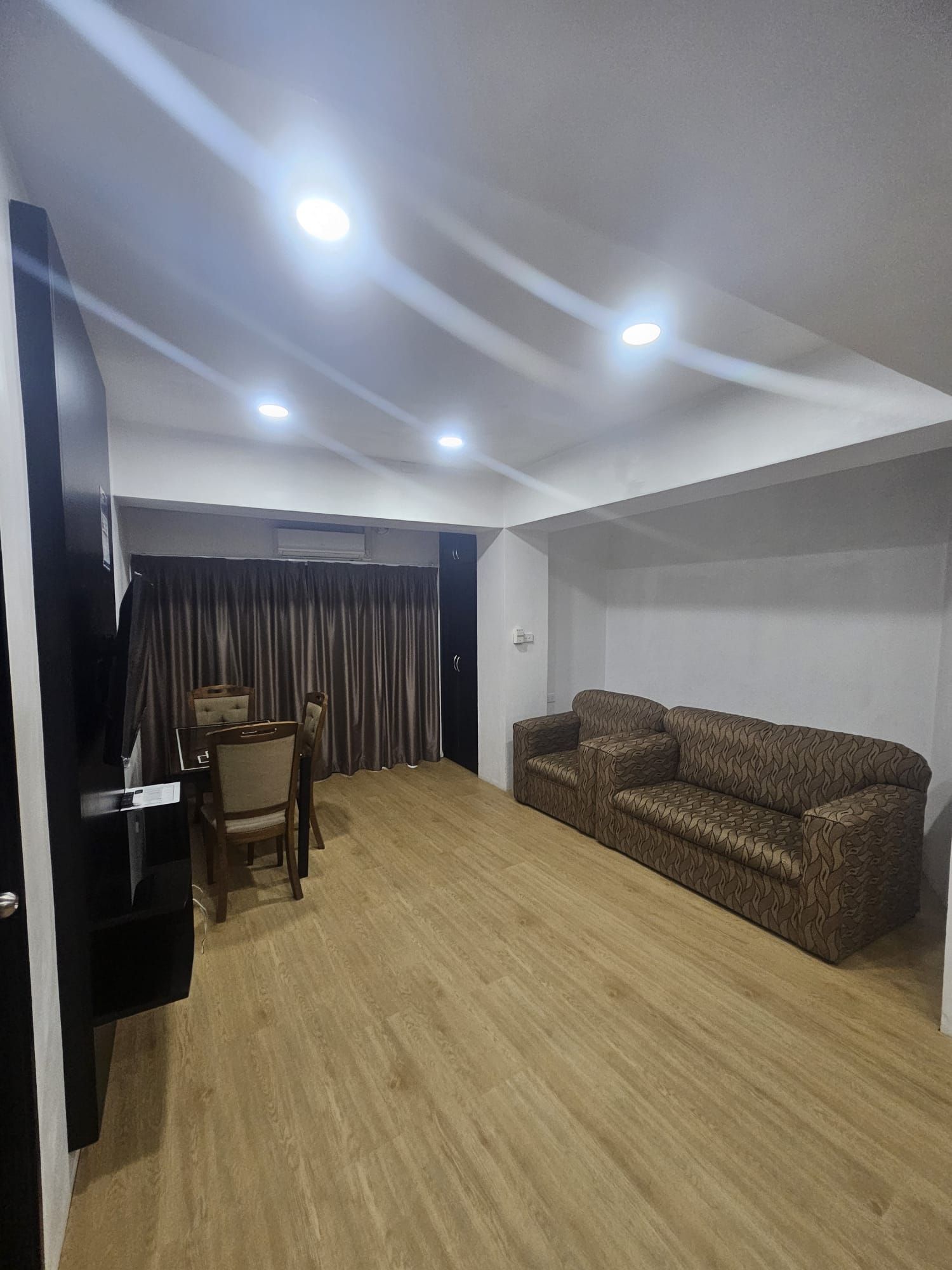 A room with a wooden floor, a brown patterned sofa, a small table with a chair, and a black cabinet.
