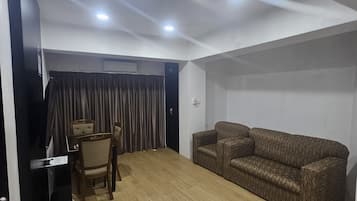 A room with a wooden floor, a brown patterned sofa, a small table with a chair, and a black cabinet.