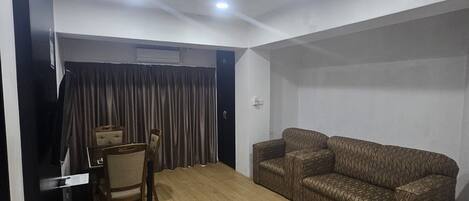 A room with a wooden floor, a brown patterned sofa, a small table with a chair, and a black cabinet.