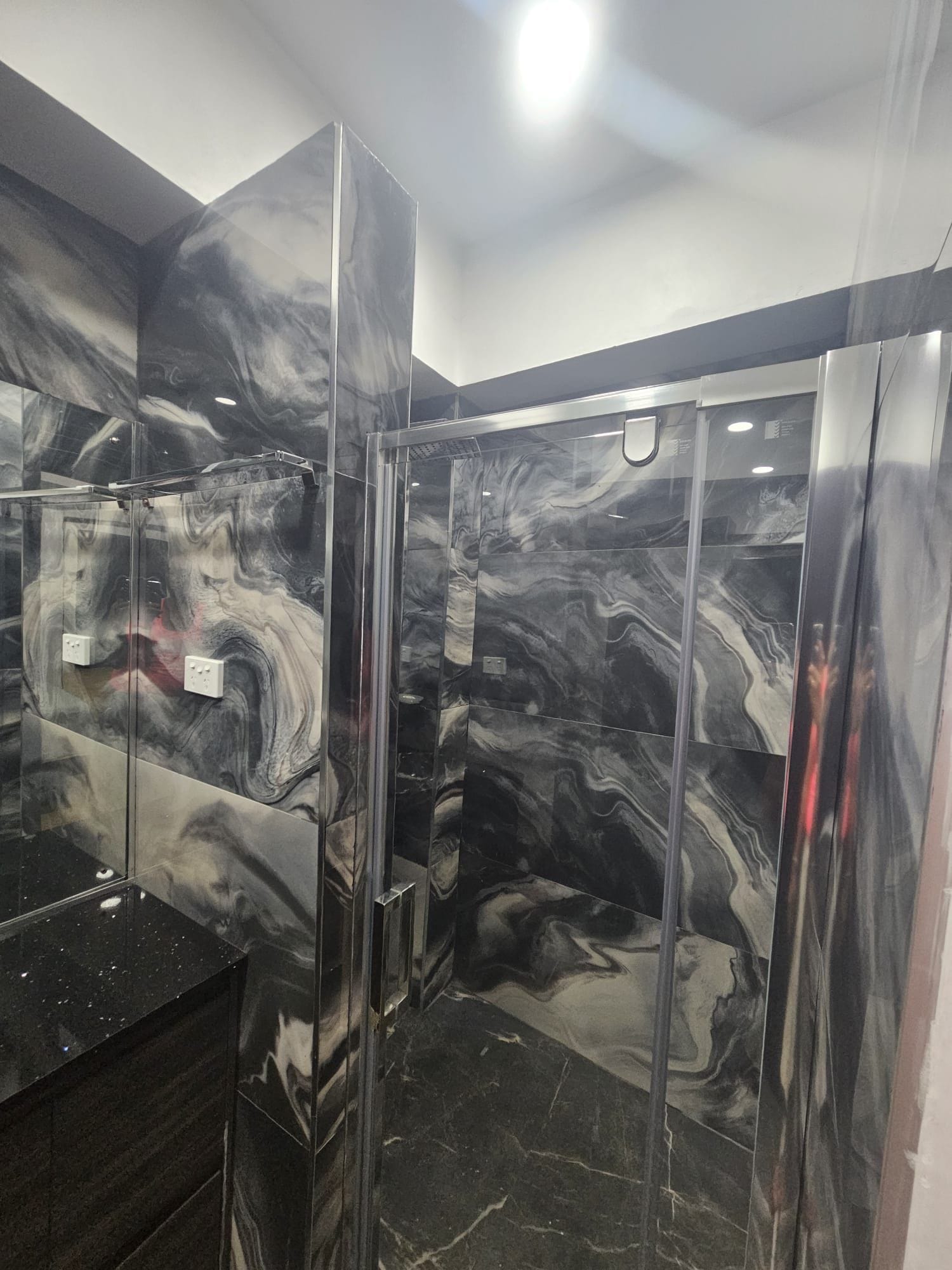A bathroom with a marble wall and a glass shower enclosure.