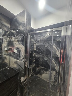 A bathroom with a marble wall and a glass shower enclosure.