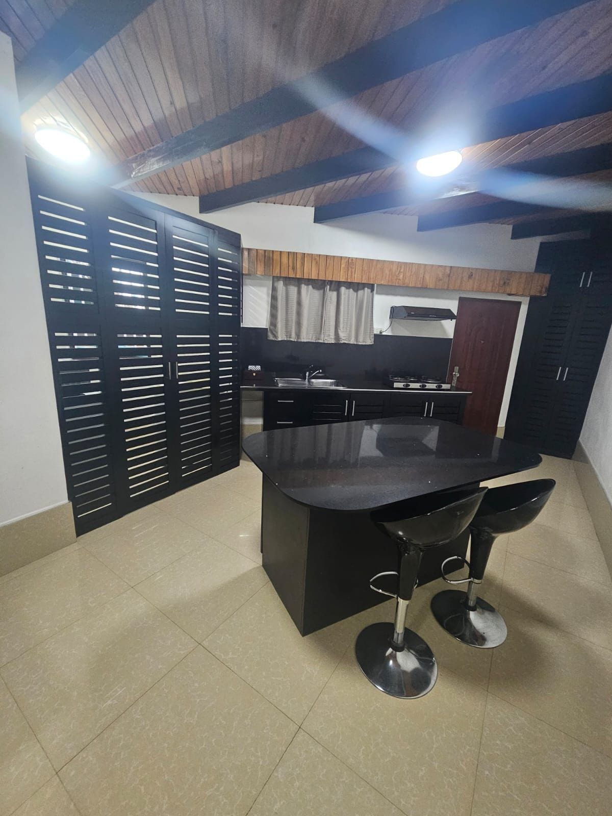 Une cuisine moderne avec un îlot central, des tabourets de bar noirs et un plafond en bois.