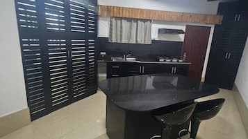 A modern kitchen with a central island, black bar stools, and a wooden ceiling.