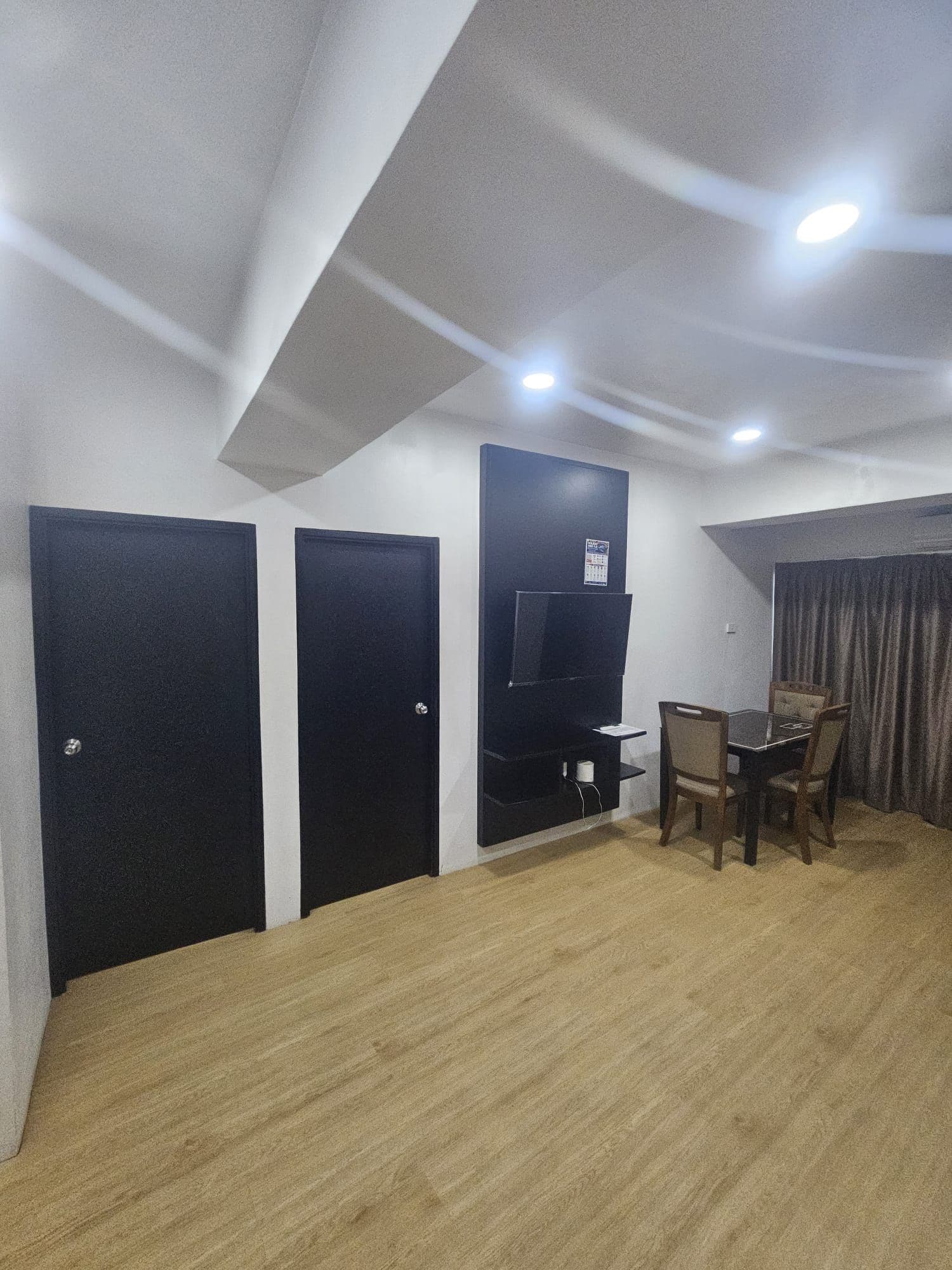 Une pièce avec un plancher en bois, une table entourée de chaises et trois portes noires.