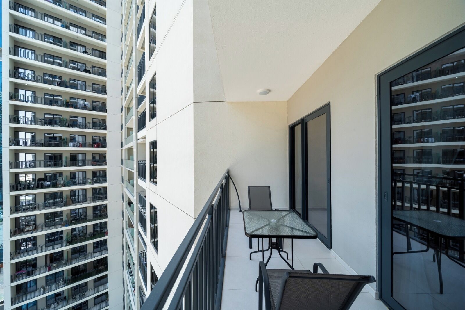 Ein Balkon mit Glasgeländer, einem Tisch und Stühlen, mit Blick auf ein Hochhaus mit mehreren Balkonen.