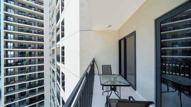 A balcony with a glass railing, a table, and chairs, overlooking a high-rise building with multiple balconies. - 2-bedroom apartment in peaceful Buiness Bay with fitness room and AC (Buiness Bay)