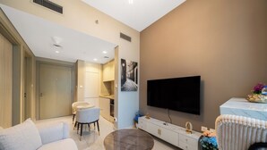A modern living room with a sofa, a round coffee table, a TV mounted on the wall, and a kitchen area in the background. - 2-bedroom apartment in peaceful Buiness Bay with fitness room and AC (Buiness Bay)