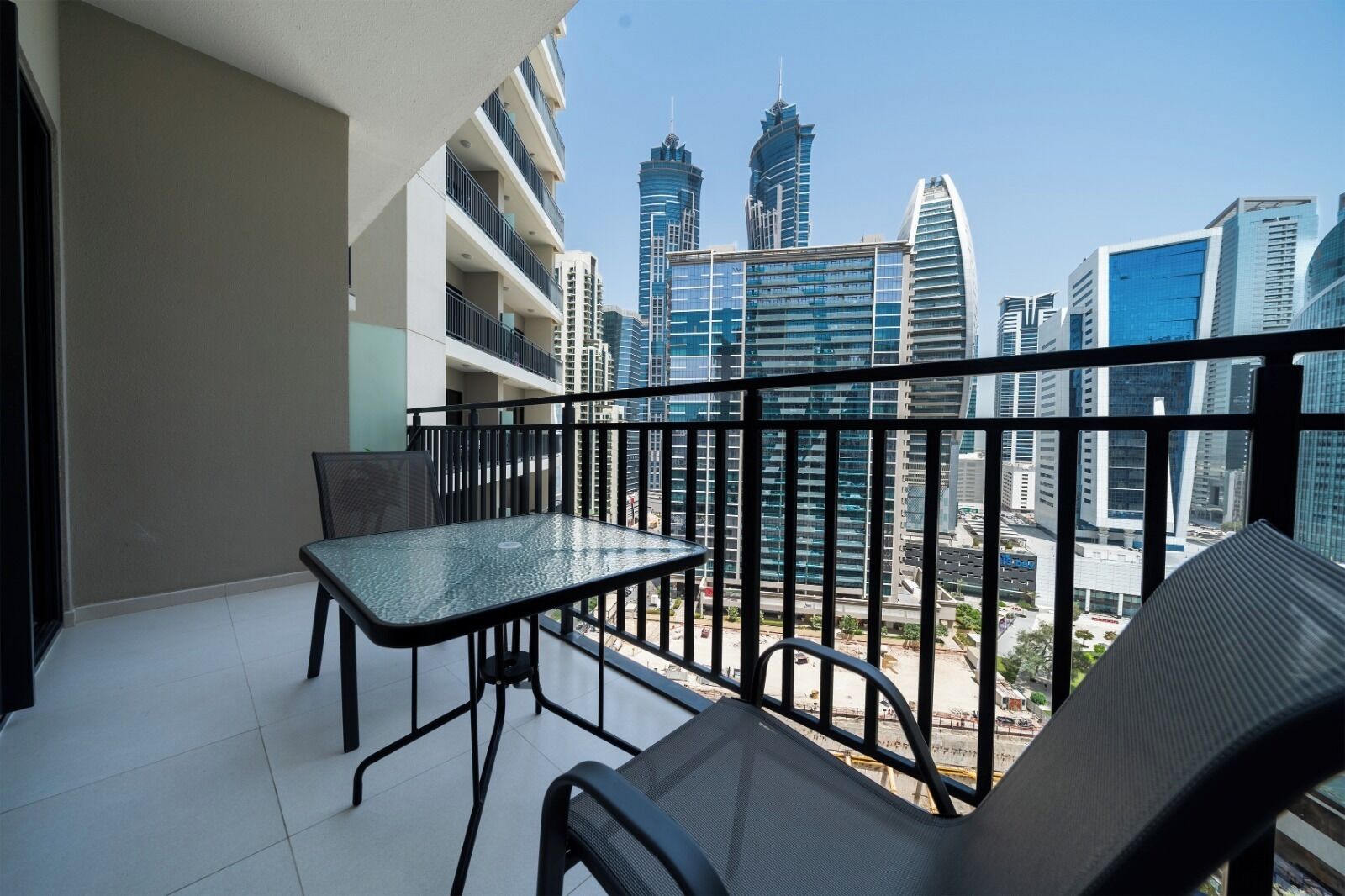 Un balcón con mesa y sillas, con vistas a modernos edificios de gran altura.
