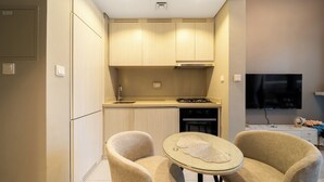 A compact kitchen with a dining area, including a small table and two chairs, a TV mounted on the wall, and a built-in oven. - 2-bedroom apartment in peaceful Buiness Bay with fitness room and AC (Buiness Bay)