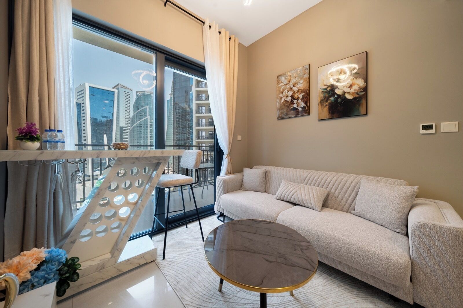 A modern living room with a sofa, a round coffee table, and a balcony with a view of city buildings.