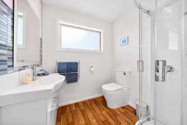 A bathroom with a white sink, a toilet, a shower, and a window.
