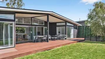 A modern house with a covered patio, a lawn, and a dining area with outdoor furniture.