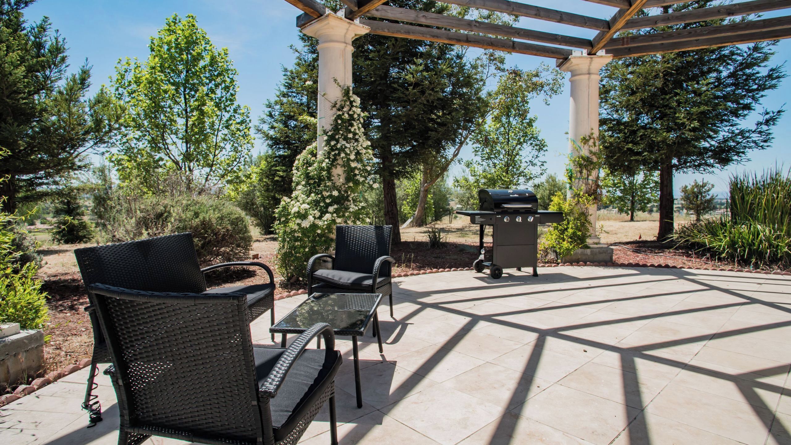 Un patio exterior con mobiliario de mimbre, una parrilla y una pérgola.