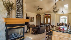 A spacious living room with a fireplace, a dining area with a glass-top table, and a kitchen with a large window. - Uvae Vineyard by Avantstay Jetted Tubs + BBQ Patios Paso Wine Country (Paso Robles)