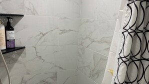 A bathroom with a shower, a hand dryer, and a shelf with toiletries.