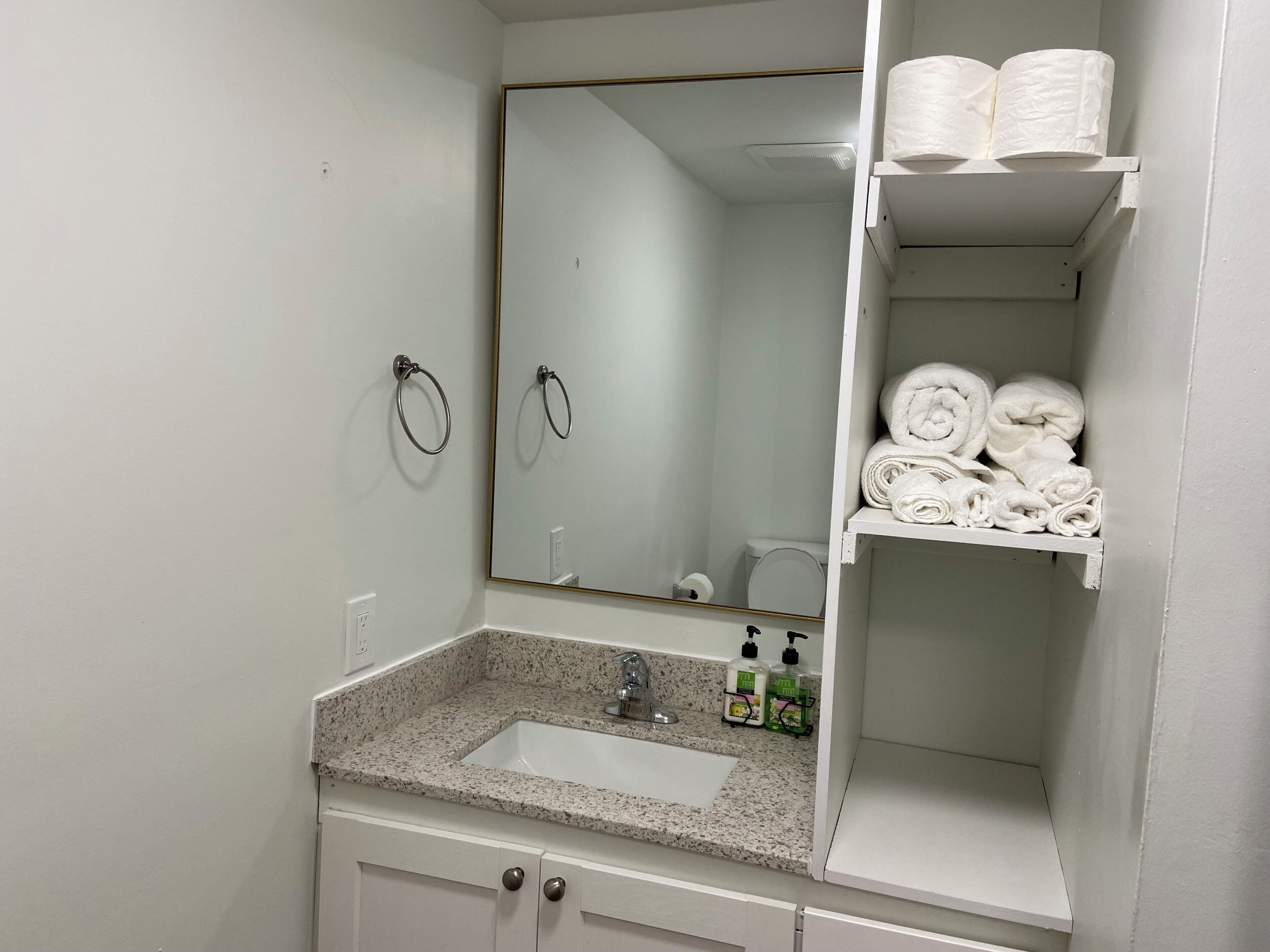 A bathroom with a sink, mirror, towel rack, and shelves with towels.