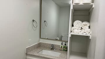 A bathroom with a sink, mirror, towel rack, and shelves with towels.