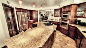 A kitchen with a large granite island, stainless steel appliances, wooden cabinets, and pendant lighting. - Candlewood Creek by Avantstay Pool + Fire Pit Quiet Paso Cul-de-sac (Paso Robles)
