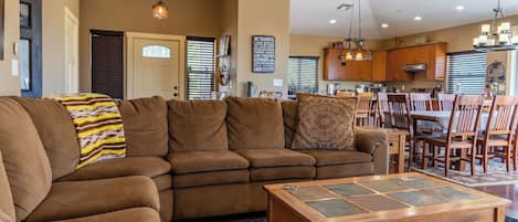 A living room with a brown sectional sofa, a coffee table with a stone top, and a dining area with wooden chairs and a table.
