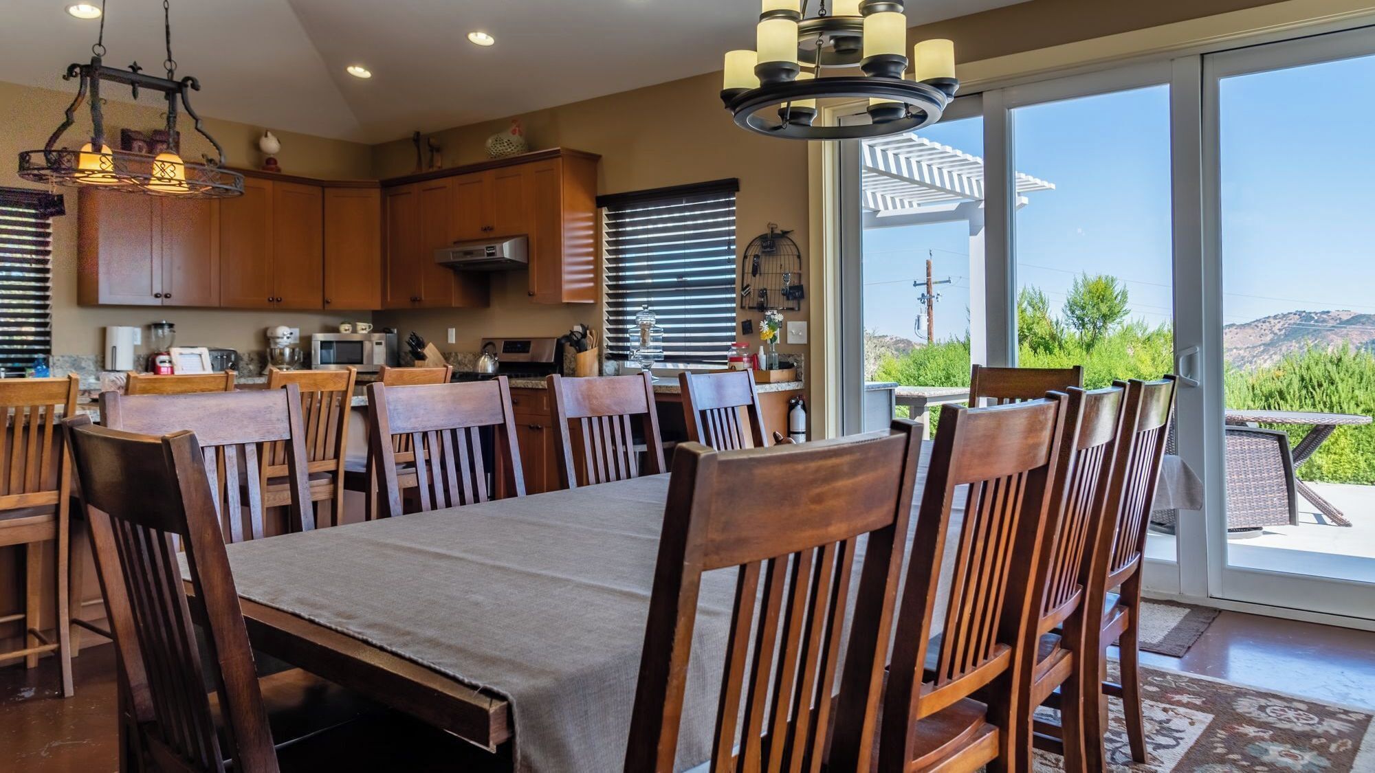 A dining area with a large table and chairs, a kitchen with wooden cabinets, and a view of the outdoors.
