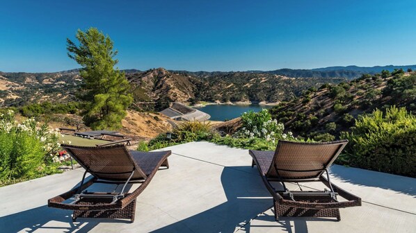 Two wicker lounge chairs facing a scenic view of a lake surrounded by hills. - Hope's Place by Avantstay Hilltop Views + Game Room Near Lake Nacimiento (Paso Robles)