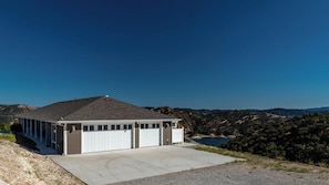 A single-story building with a garage, a covered porch, and a view of a lake and hills. - Hope's Place by Avantstay Hilltop Views + Game Room Near Lake Nacimiento (Paso Robles)