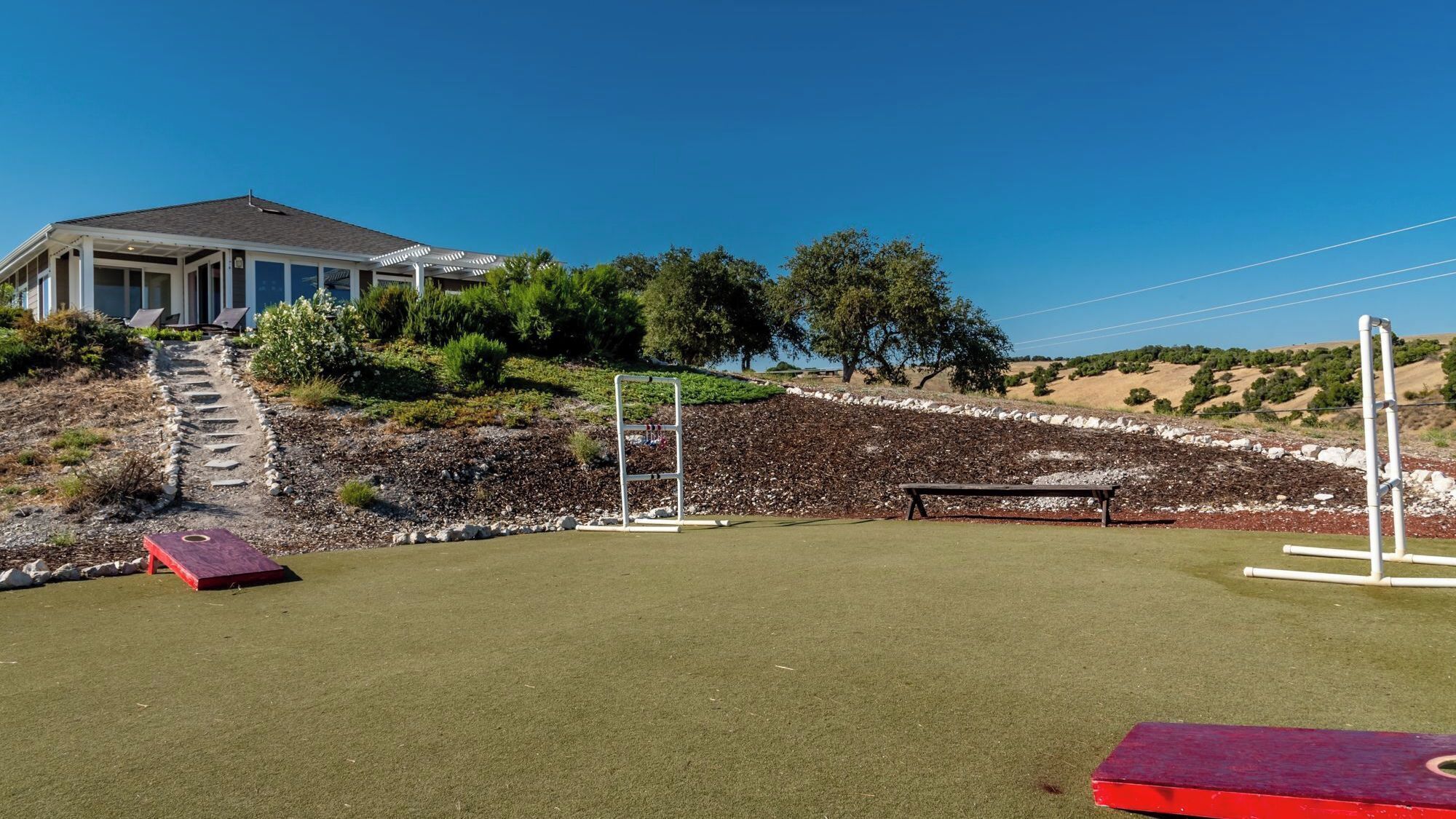 A golf course with a house in the background, a red bench, and a white structure.