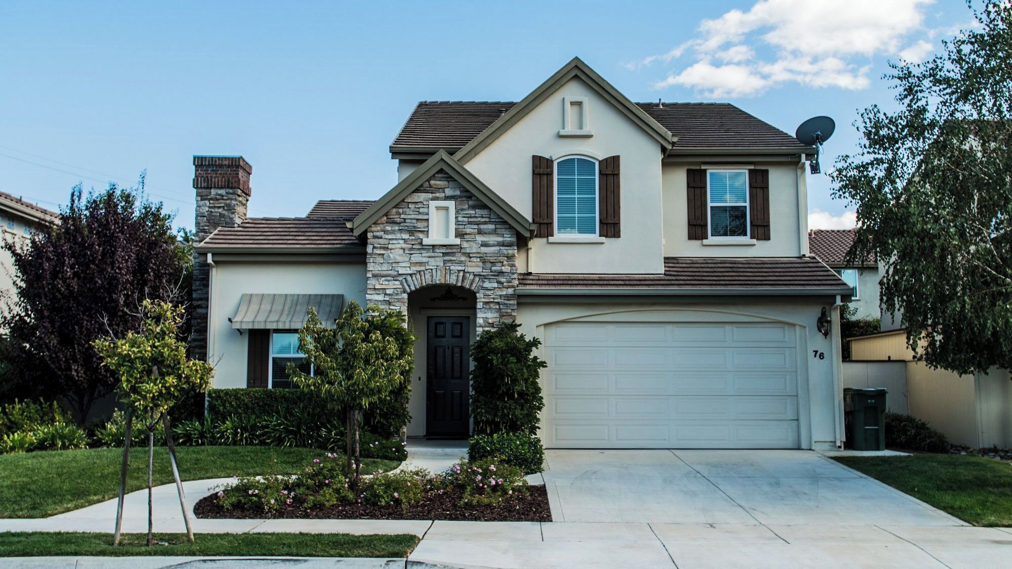 A two-story house with a stone facade, a garage, and a well-maintained front yard.
