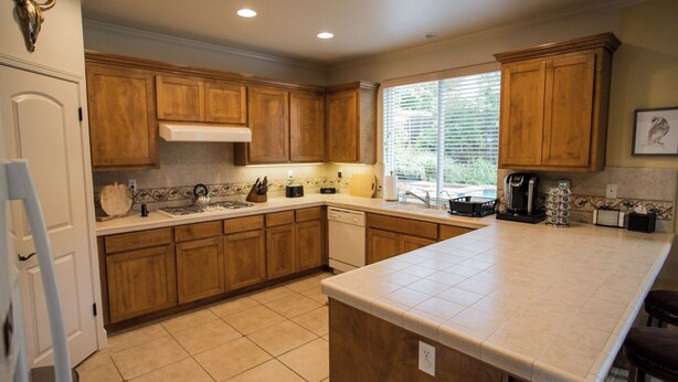 A kitchen with wooden cabinets, a large island, a dishwasher, and a coffee maker. - Navajo Trail by Avantstay Lap Pool + Spa Steps to Salinas River Trail (Paso Robles)