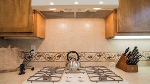 A kitchen with a gas stove, a kettle, a knife block, and a decorative backsplash. - Navajo Trail by Avantstay Lap Pool + Spa Steps to Salinas River Trail (Paso Robles)