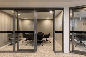 Una sala de reuniones con puertas de vidrio, una mesa y sillas de oficina.