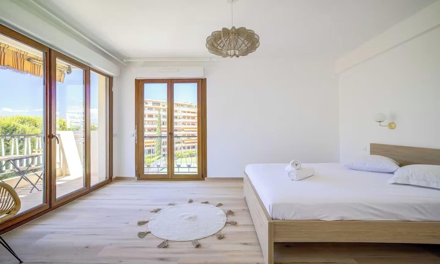 A bedroom with a large bed, a round rug, and a view through a sliding glass door.