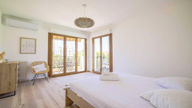Un dormitorio con una cama grande, un aparador de madera, una silla y un balcón con vistas.