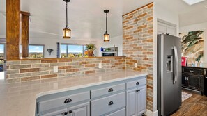 Una cocina con salpicadero de ladrillo, refrigerador de acero inoxidable e iluminación colgante.