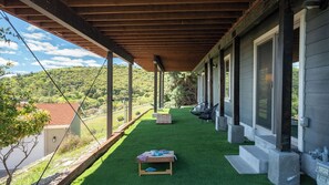 A covered outdoor area with artificial grass, a table with items on it, and a view of a hilly landscape. - Highland Park Panorama by Avantstay Game Room + Panoramic Views Wine Country (Paso Robles)