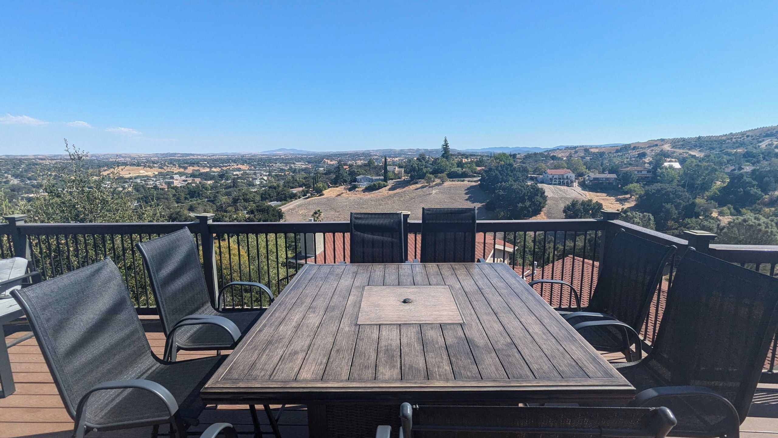 A wooden deck with a table and chairs, overlooking a residential area with houses and hills.